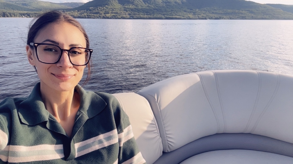 A woman wearing glasses is smiling while sitting on a boat in a lake