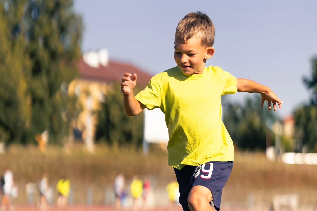 A child is running outside in athletic clothes and smiling